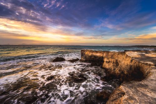 Free Stunning seascape with crashing waves and a vibrant sunset over rugged coastal cliffs. Stock Photo