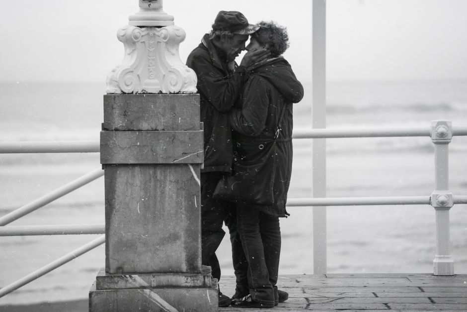 A loving couple embraces on a seaside pier, captured in black and white for timeless romance.