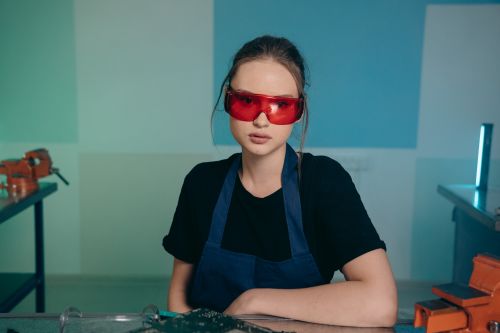 Free Woman in a workshop setting wearing safety glasses and apron, focused on manufacturing tasks. Stock Photo