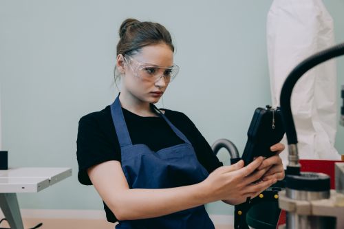 Free A woman in a blue apron uses a device in a workshop, wearing protective goggles. Stock Photo