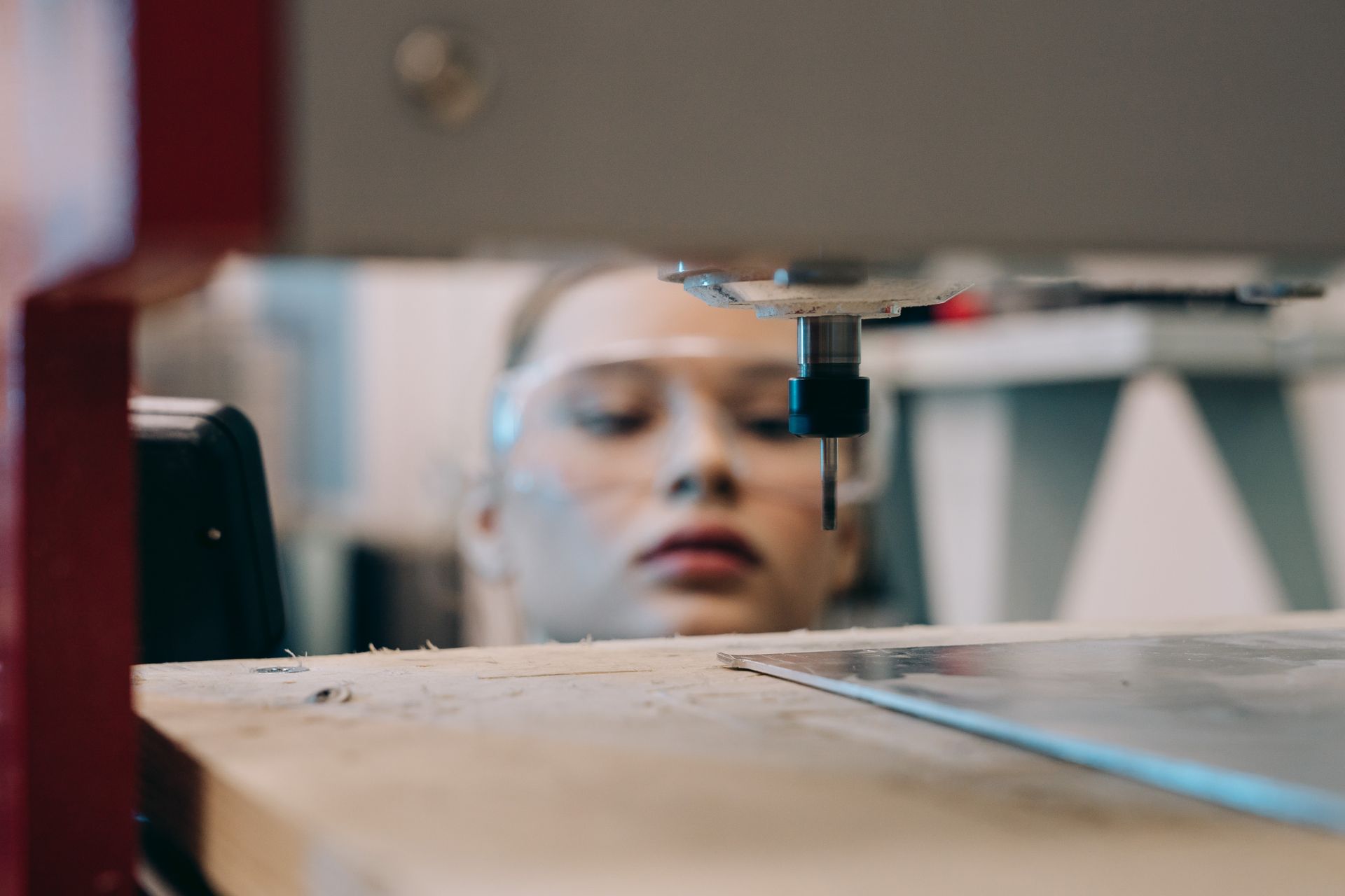 Woman wearing protective goggles working with precision technology in a workshop setting.