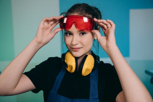 Free Smiling woman adjusting safety goggles with headphones, indoors setting. Stock Photo