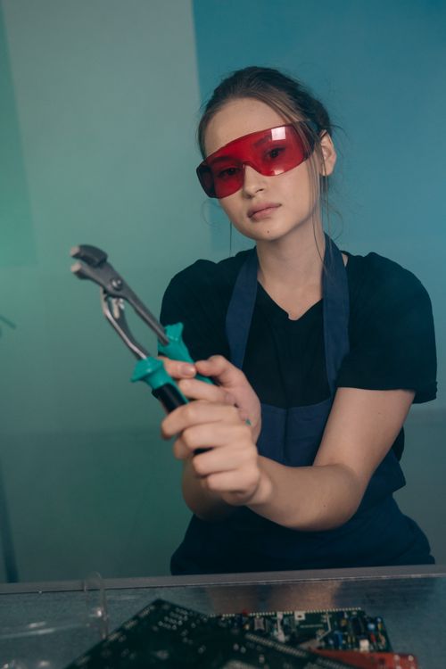 Free Young female engineer wearing red safety glasses working with tools in an indoor workshop. Stock Photo