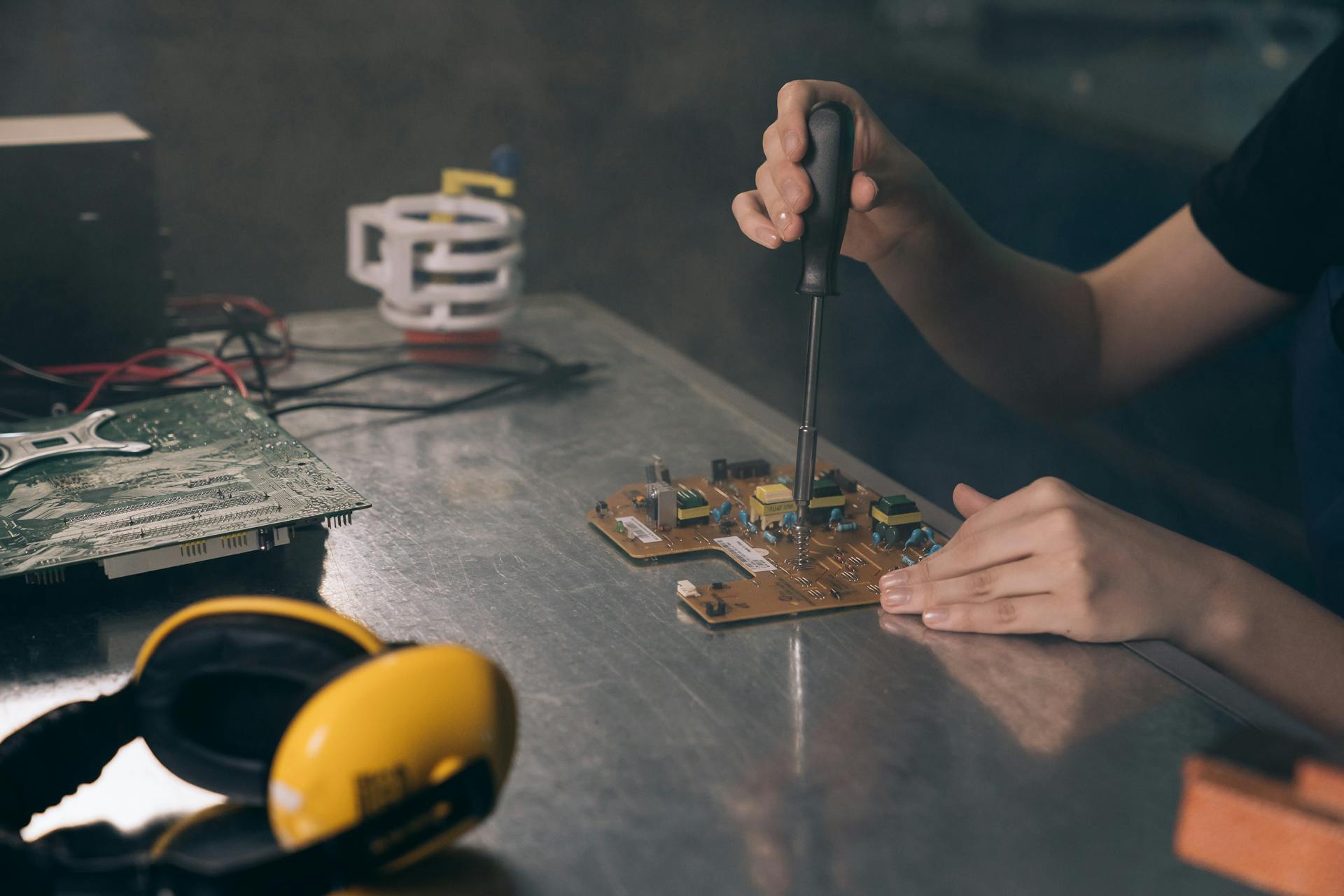 Close-up of hands working on electronic circuit board in workshop.