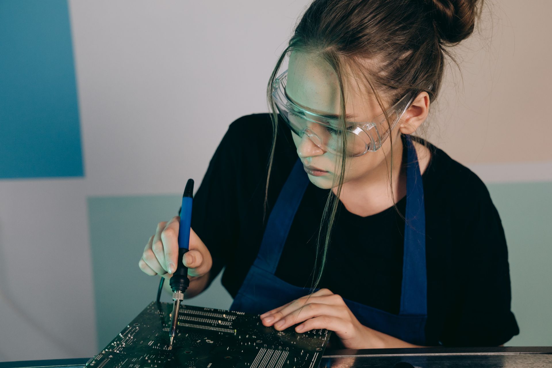 Young female engineer using a soldering iron on a circuit board, focused on electronics work.