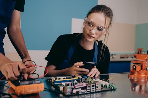 Woman in Goggles Sitting with Smartphone over Computer Hardware