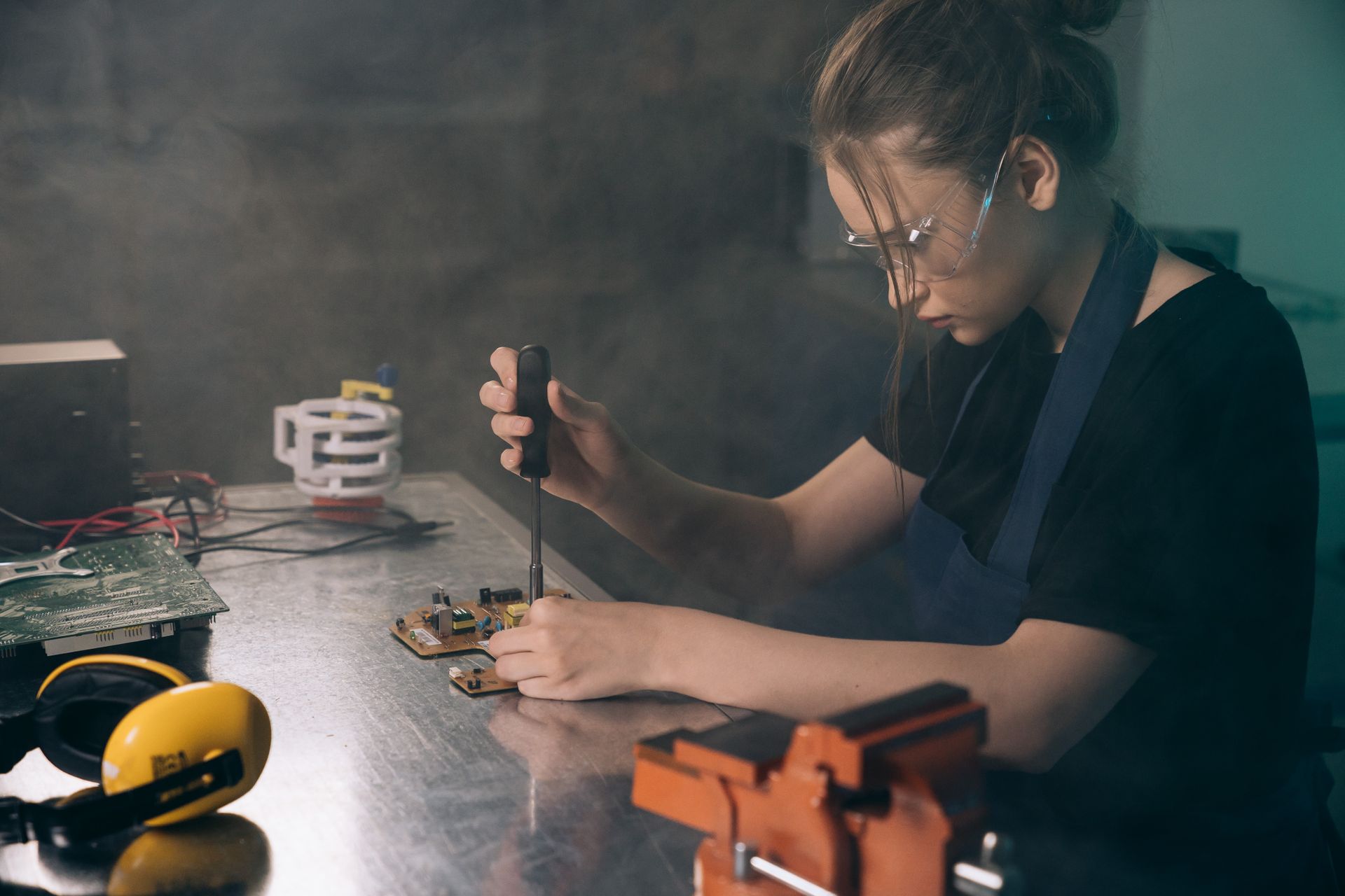 Focused young woman in workshop assembling electronic circuits with precision tools.