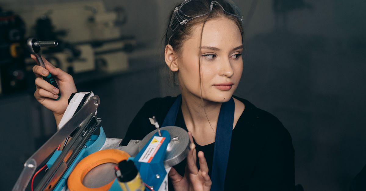Young female engineer adjusts machinery in an industrial workshop setting.