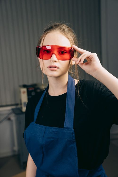 Free Portrait of a woman wearing red goggles and blue apron in an industrial workshop. Stock Photo