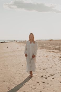 A serene scene of a woman in a white dress walking along an empty beach at sunset.