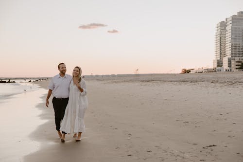 Free A Man and Woman Walking Barefoot on Beach Sand  Stock Photo