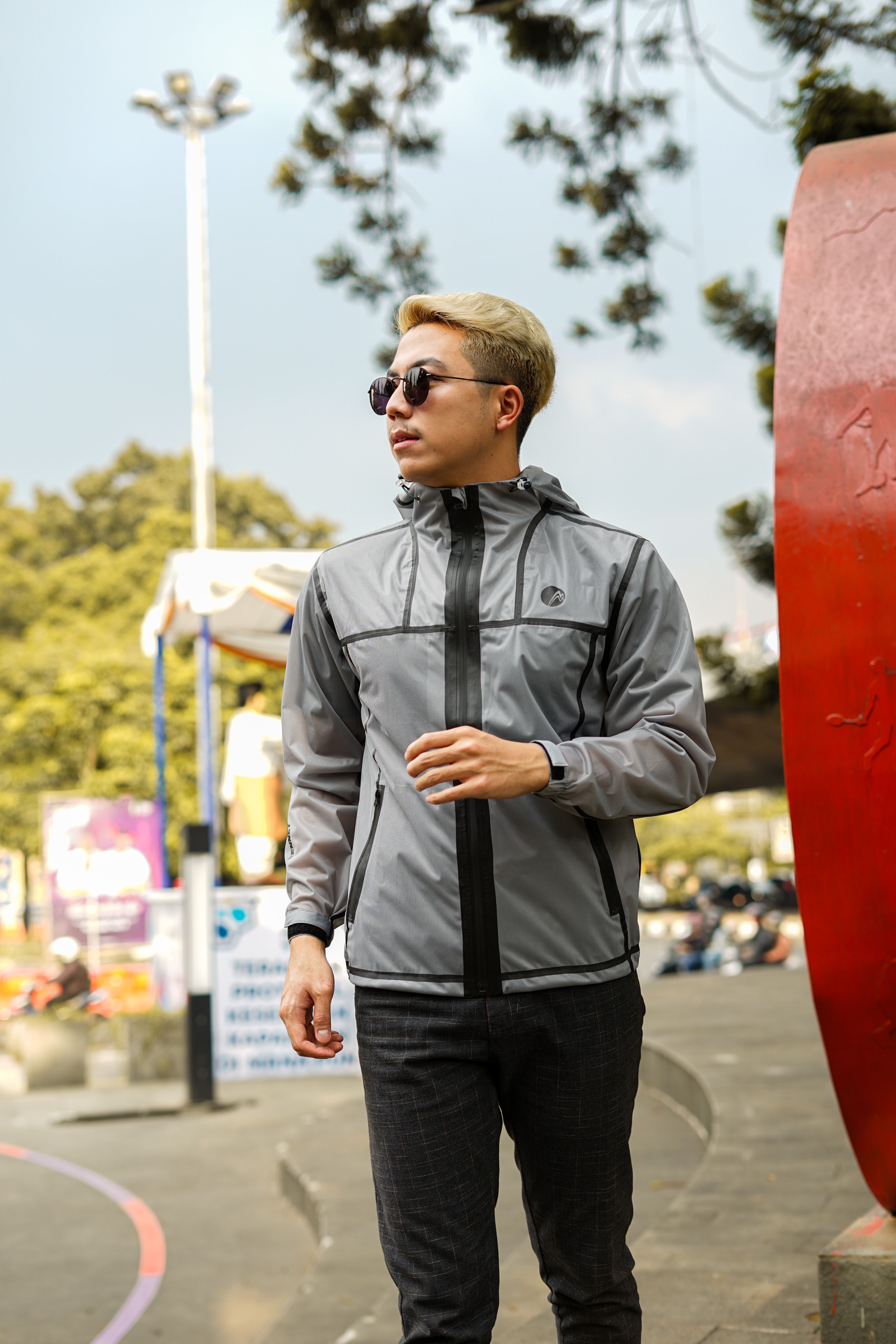 A fashionable man wearing sunglasses and a jacket strolls in a sunny outdoor setting.