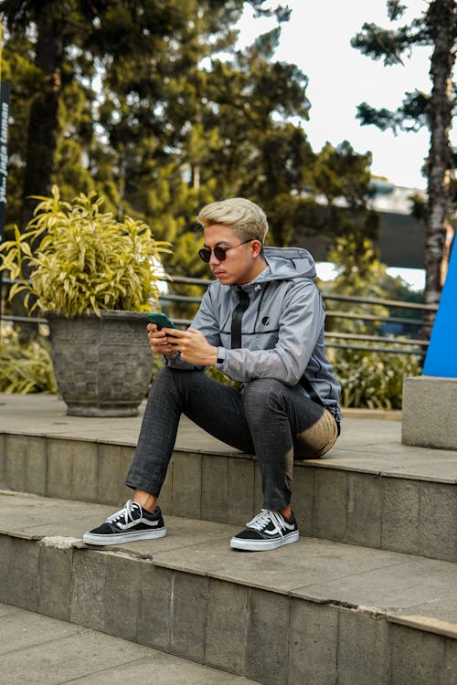 Man in Gray Jacket Holding Cellphone While Sitting on Step