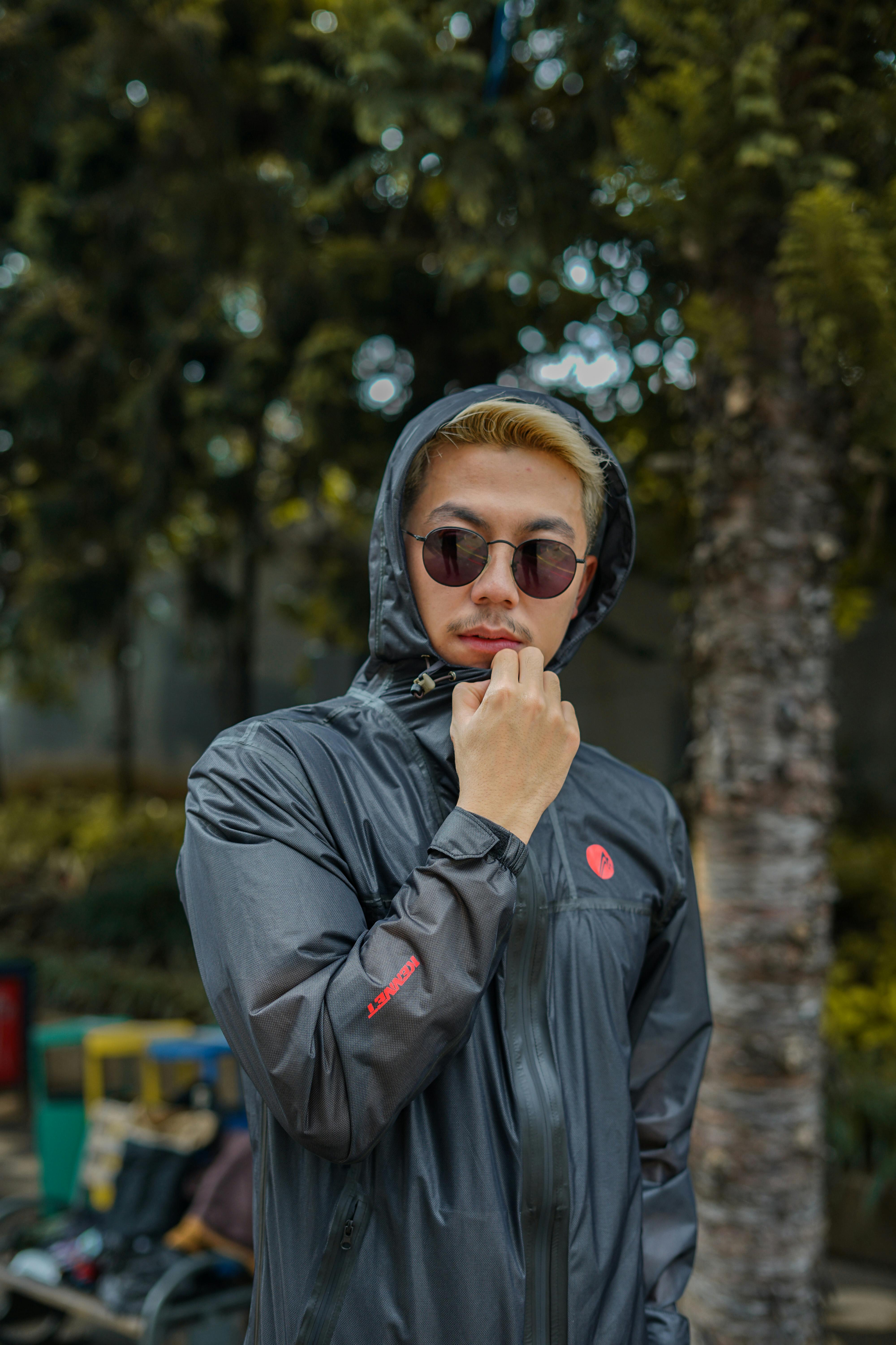 Free A fashionable man poses outdoors wearing a hoodie and sunglasses for a modern look. Stock Photo