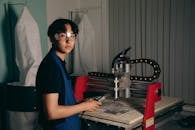A Young Man in an Apron and Safety Glasses Standing by a CNC Machine