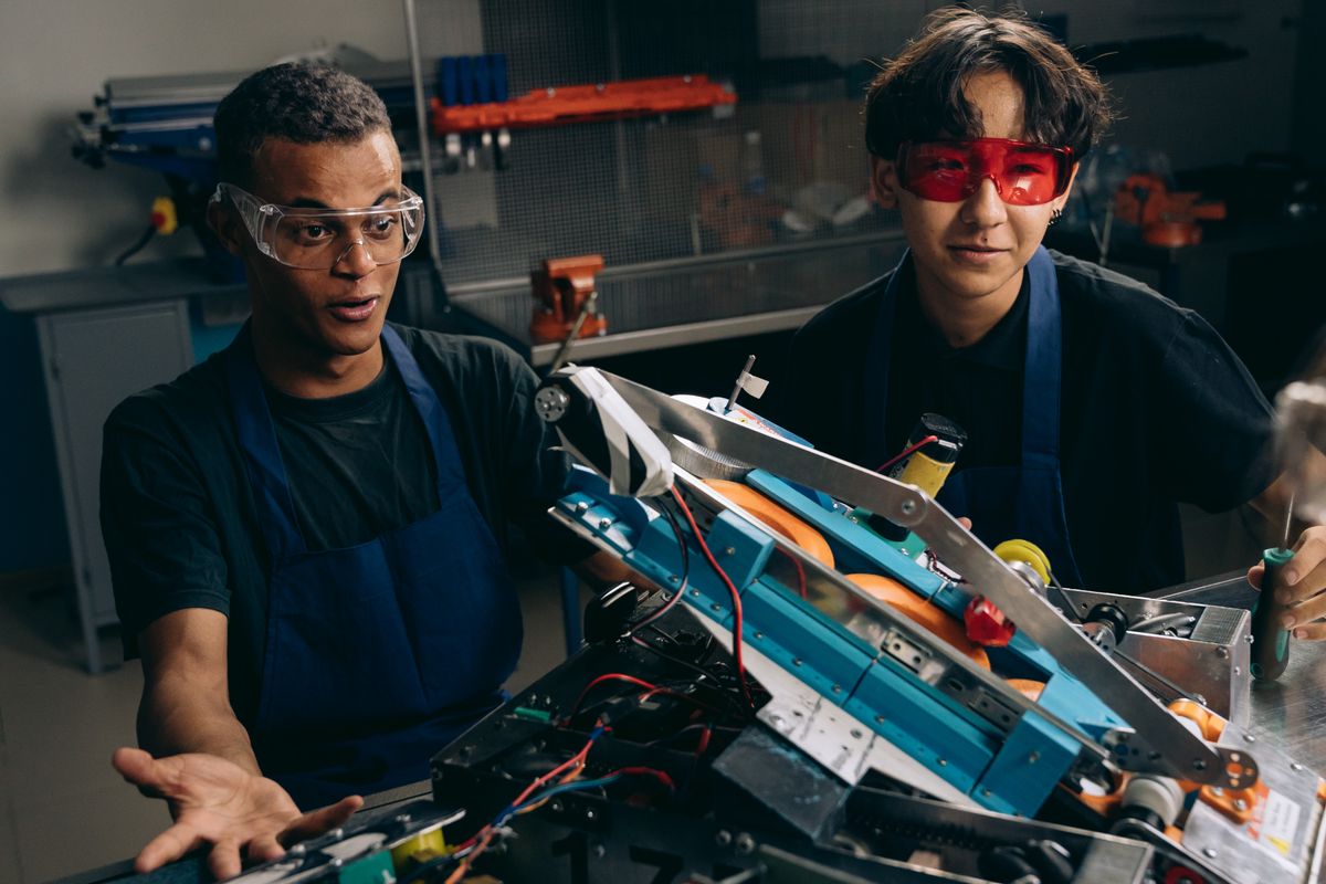 Two engineers wearing safety goggles closely evaluating a working prototype in a workshop
