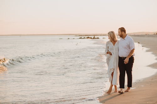 Free Couple strolling along a serene beach during sunset, enjoying a peaceful moment. Stock Photo