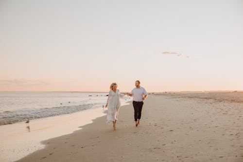 A Couple Walking on a Seashore while Holding Hands