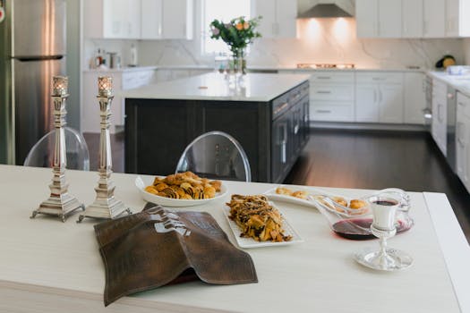 A modern kitchen setup featuring a Sabbath table with baked goods, candles, and wine.
