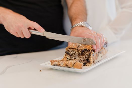 Close-up of hands slicing fresh chocolate babka bread on a white platter.