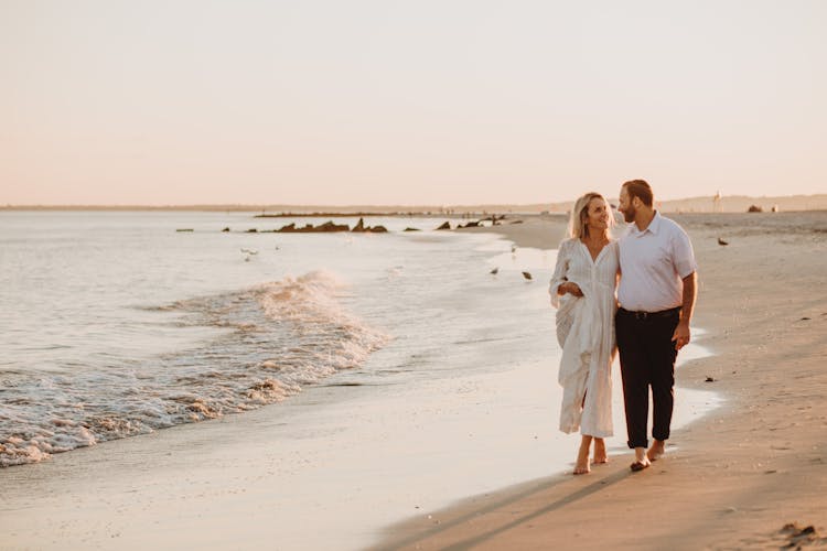 A Couple Walking Side By Side On The Beach Shore