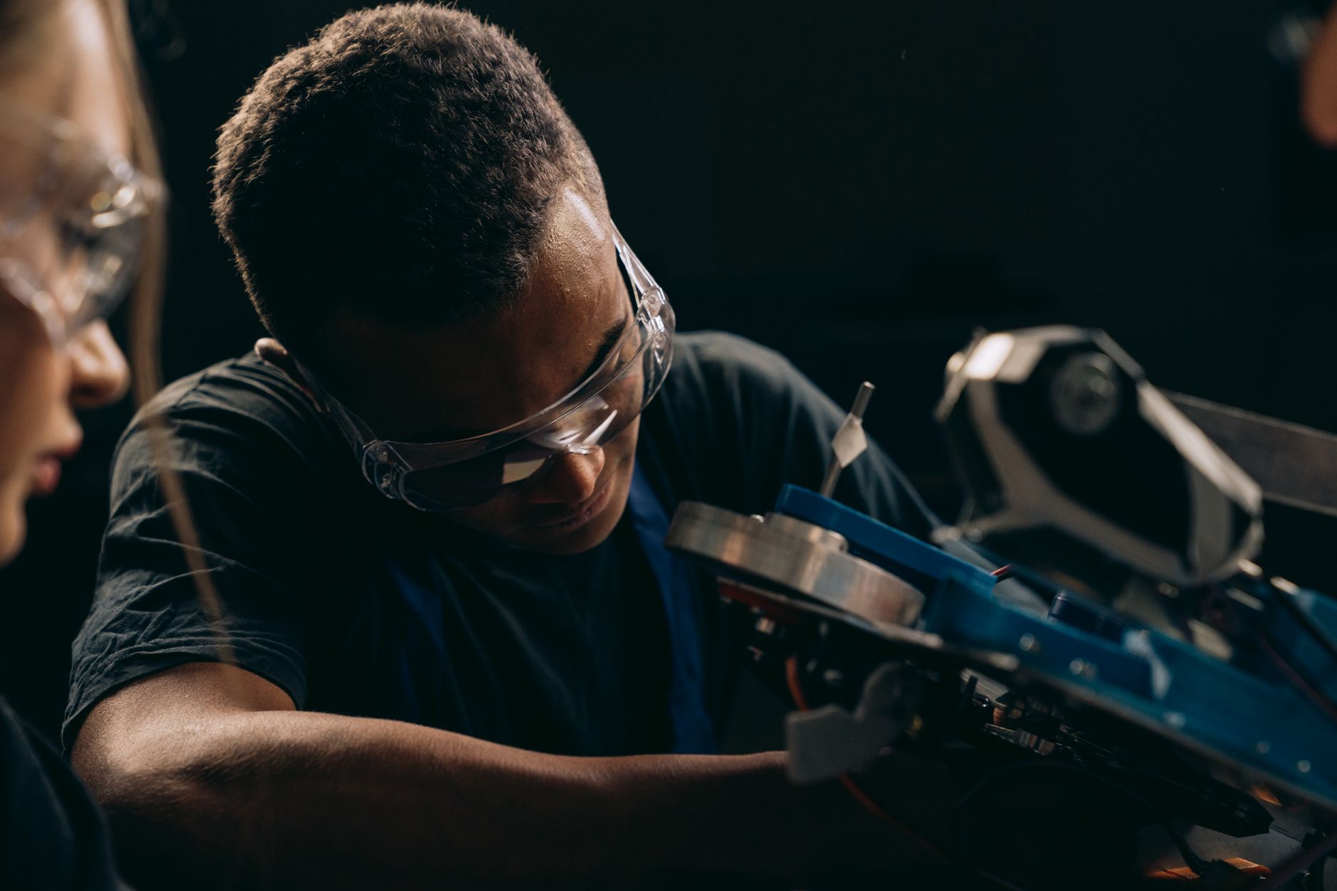 Focused engineer working on machinery in a dimly lit workshop, wearing safety goggles.
