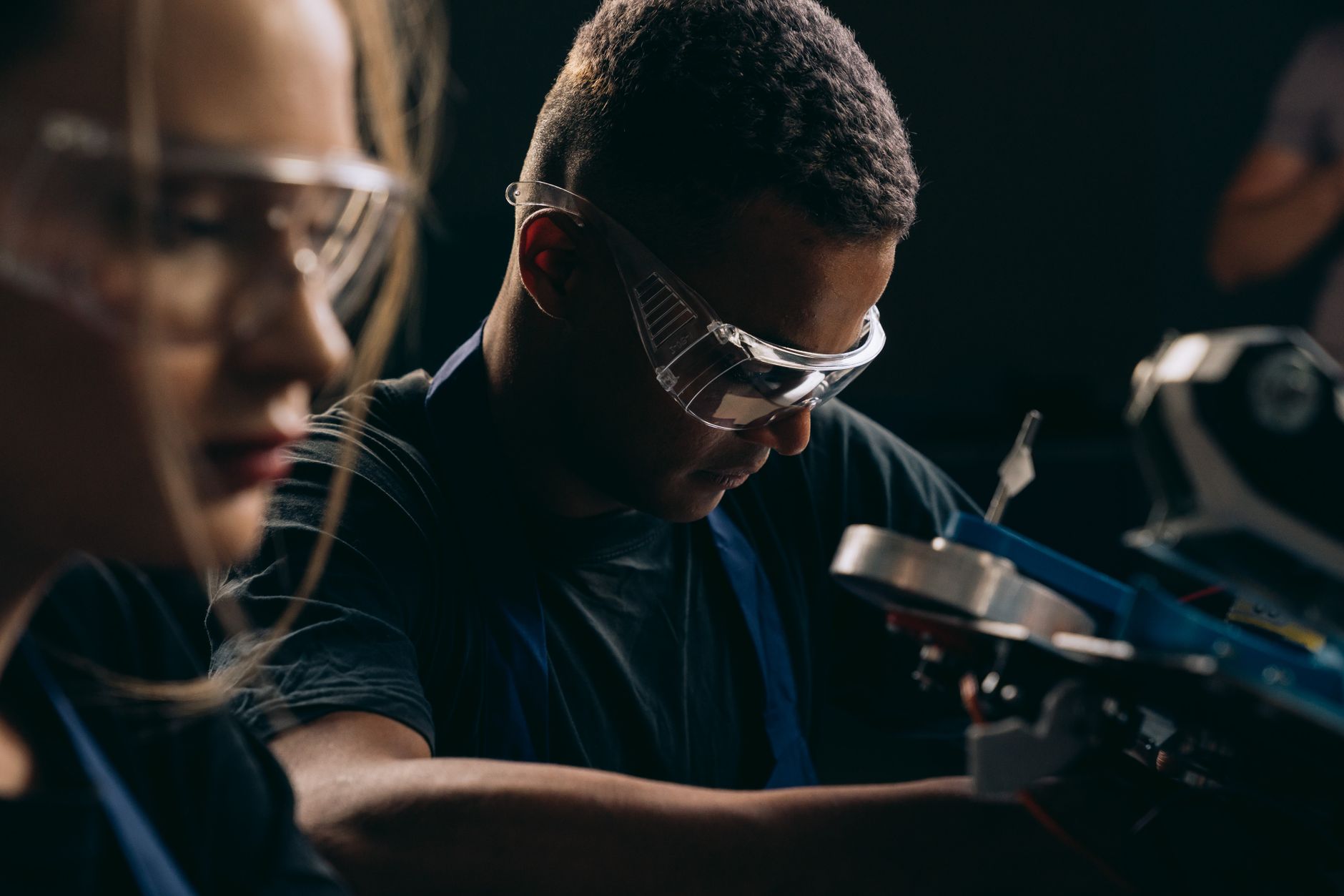 Students focused on robotics, wearing protective goggles, symbolizing teamwork and education in technology.