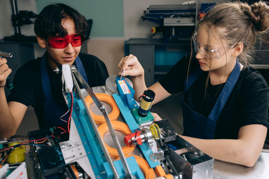 テックラボでロボットプロジェクトに取り組む2人の学生が、機械の詳細に焦点を当てています。
