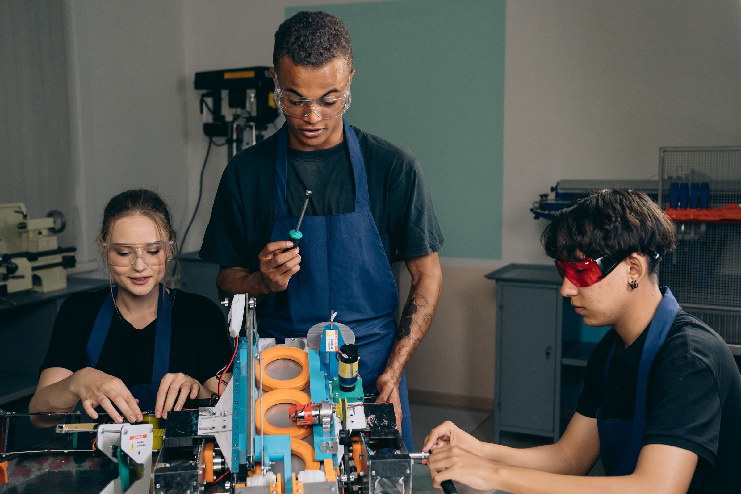 Group of adults wearing workshop aprons and safety glasses while collaborating with tools and project equipment