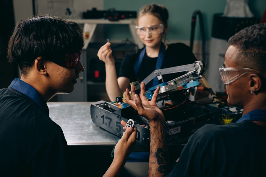 Three engineers collaborating on a robotics assembly in a workshop, photo by Mikhail Nilov on Pexels