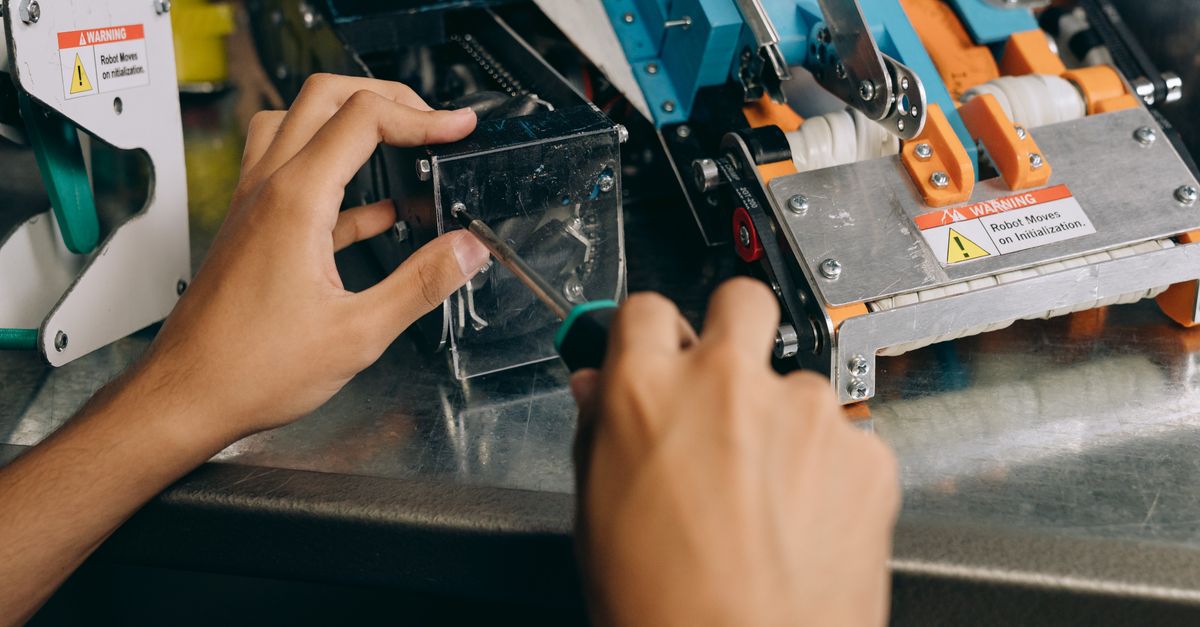 Hands of a technician repairing robotic machinery with precision tools on a workbench.