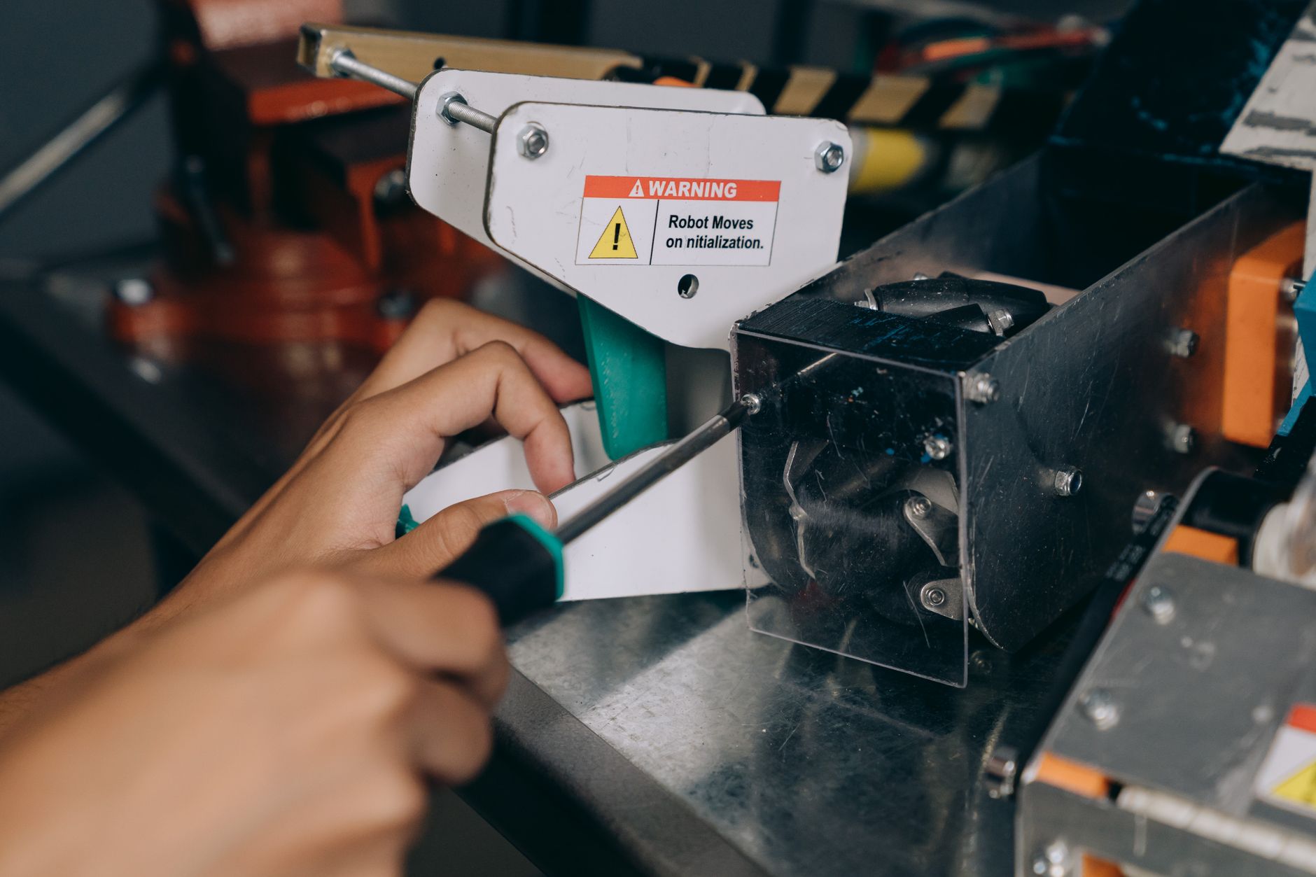 Close-up of a hand using a screwdriver to fix industrial robot machinery indoors.
