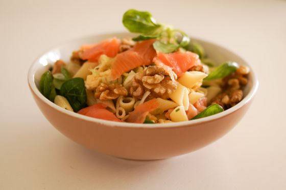 Bowl of penne pasta salad with smoked salmon ribbons, walnut halves and lamb's lettuce