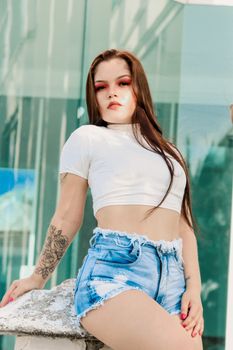 Confident woman posing in a crop top and denim shorts with modern architecture background.