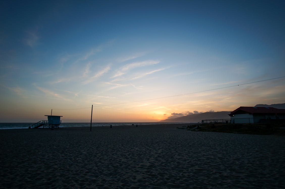 免费 蓝蓝的天空，日出时的棕色云下的海滨 素材图片