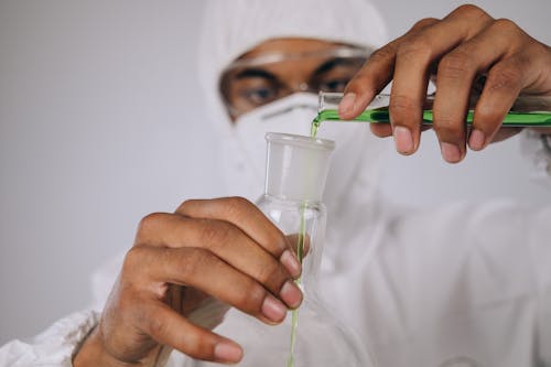 Free A Person Wearing Personal Protective Equipment Pouring Green Chemical on Florence Flask from Test Tube Stock Photo