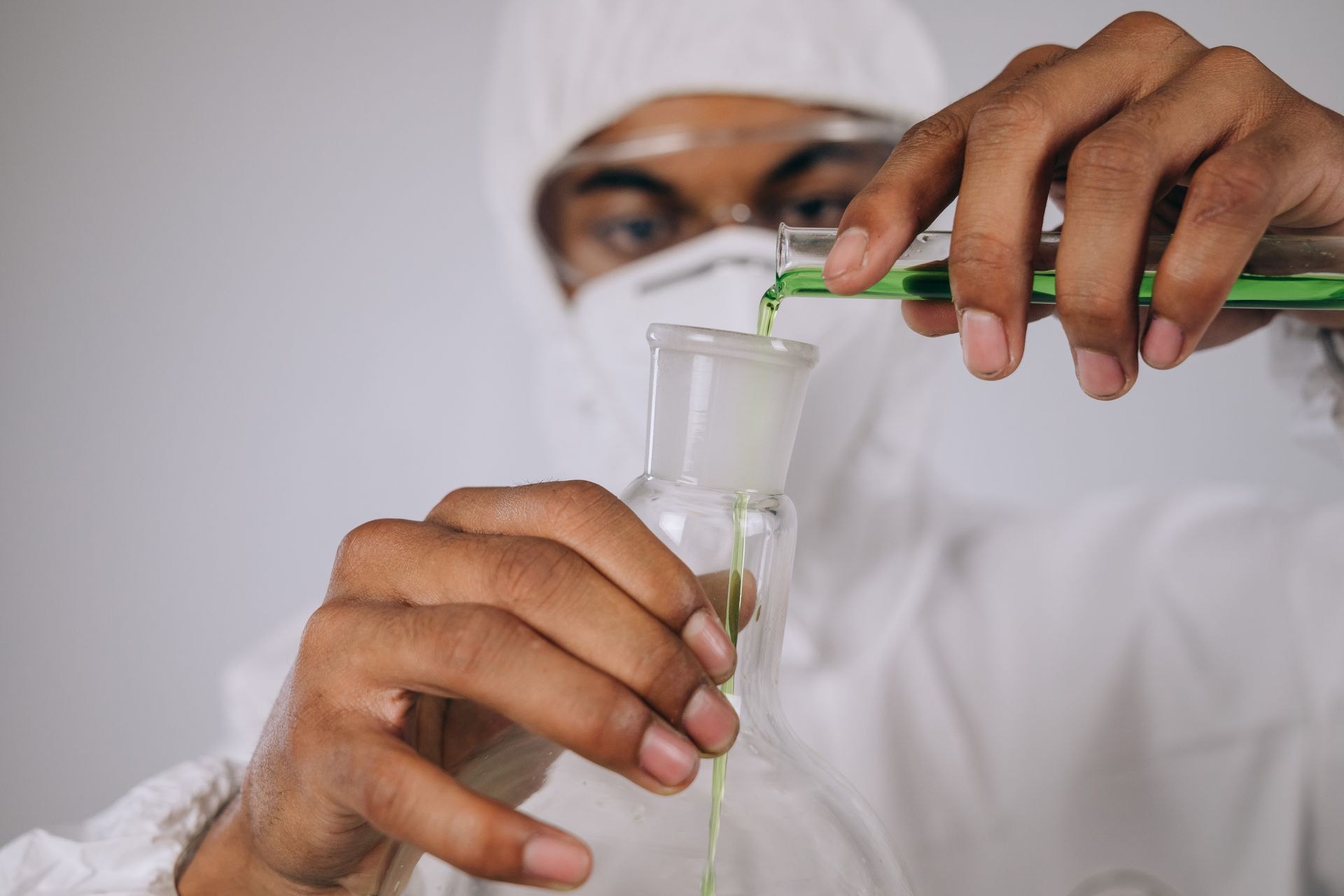A Person Wearing Personal Protective Equipment Pouring Green Chemical on Florence Flask from Test Tube