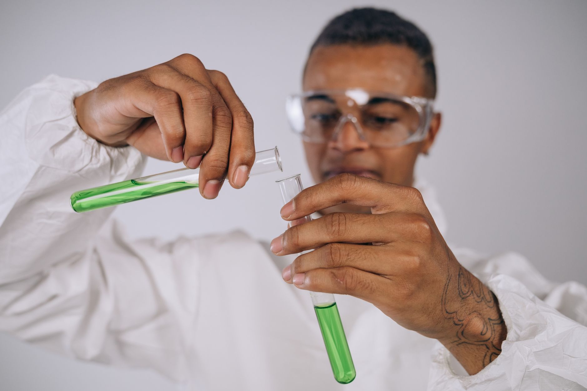 A scientist conducts an experiment indoors, transferring green liquid between test tubes.