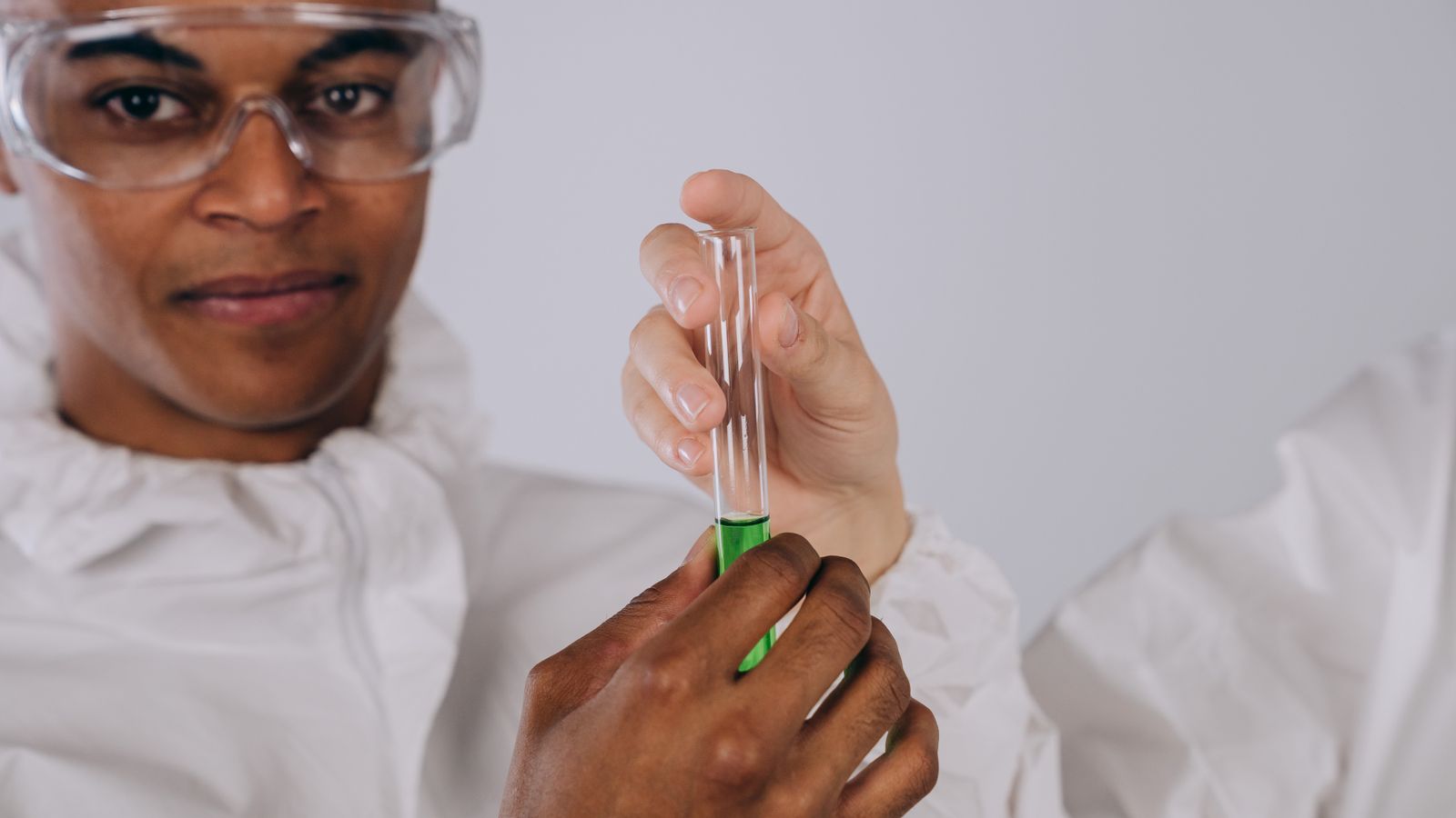 A scientist in protective gear conducting an experiment with a test tube in a lab setting.