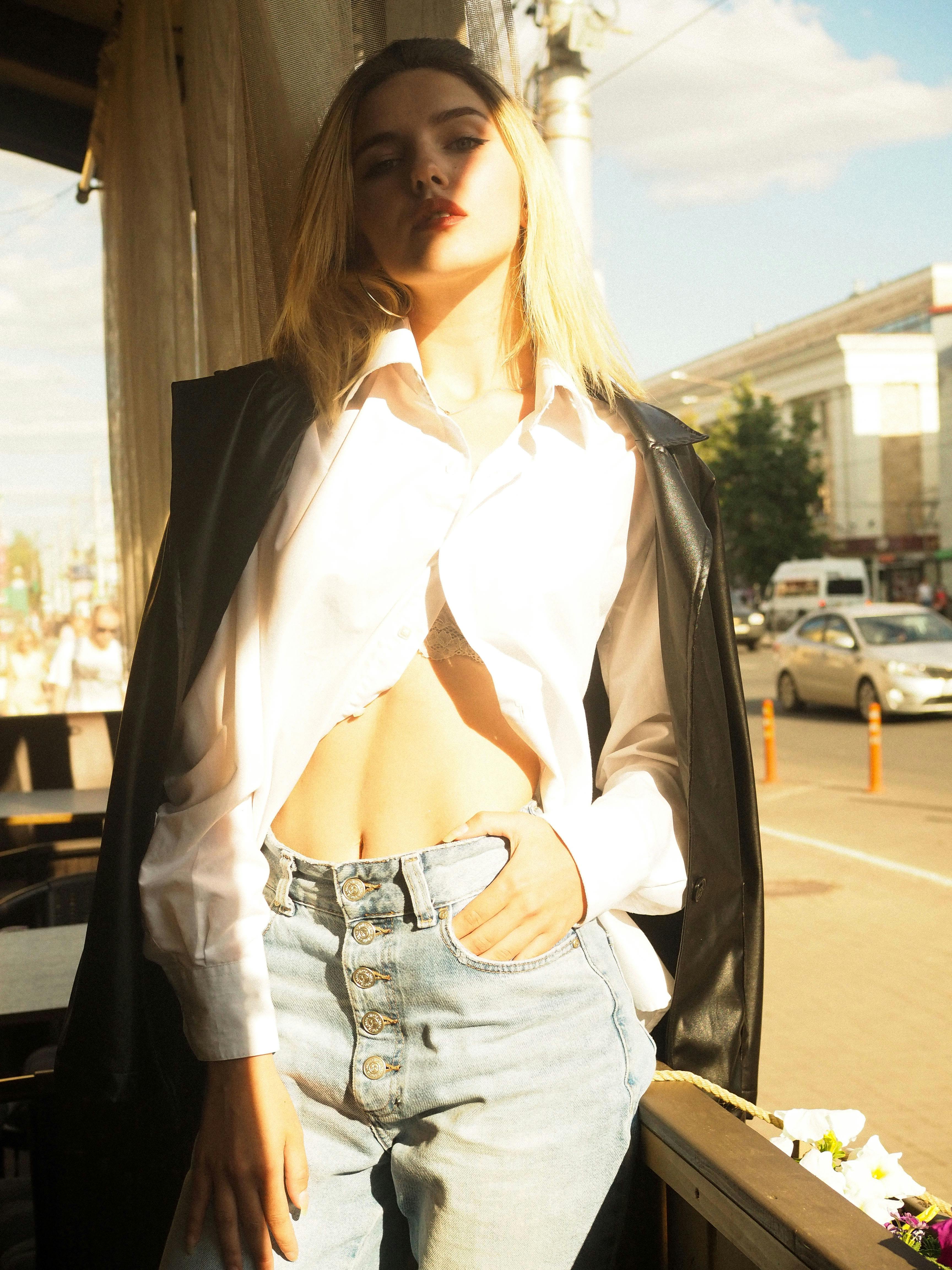 Stylish woman posing in denim and leather jacket, exuding modern fashion in an urban setting.
