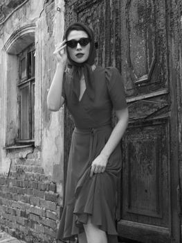 Elegant woman in vintage attire with sunglasses, posed against an old brick wall.