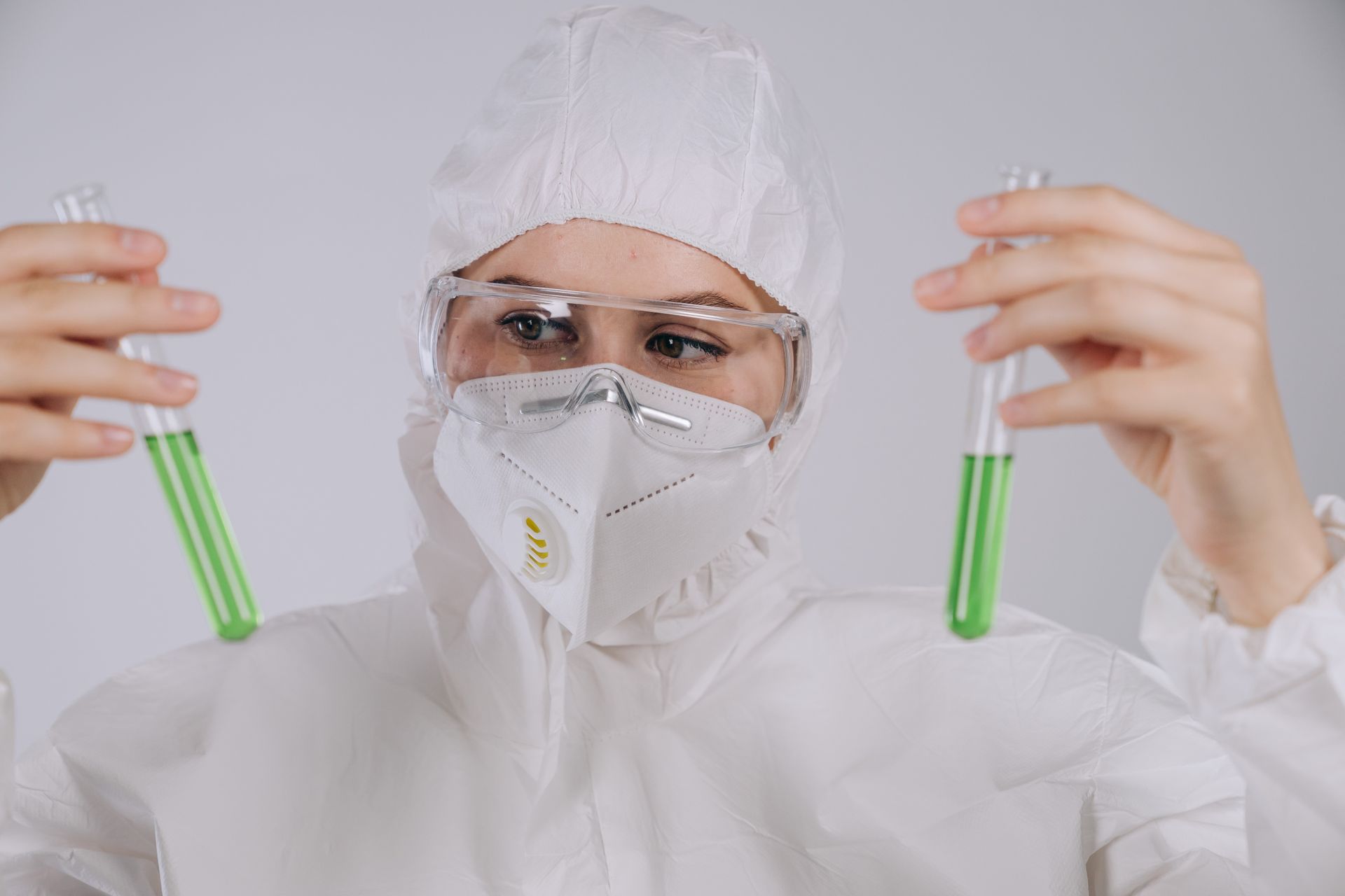 A Person in Safety Glasses and Personal Protective Equipment Looking at the Test Tube with Chemical she is Holding