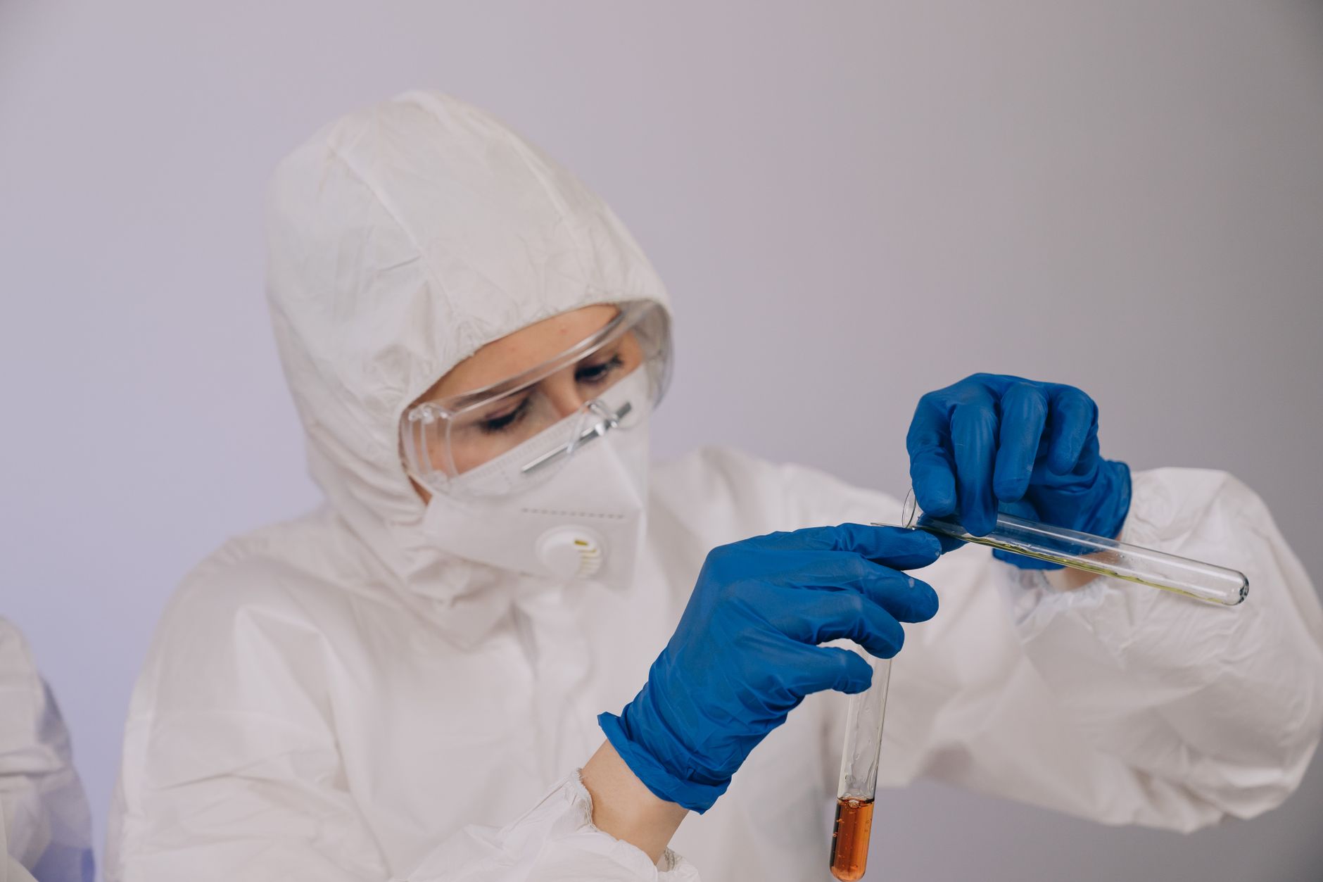 Scientist in PPE and gloves carefully handling test tubes in a laboratory setting.