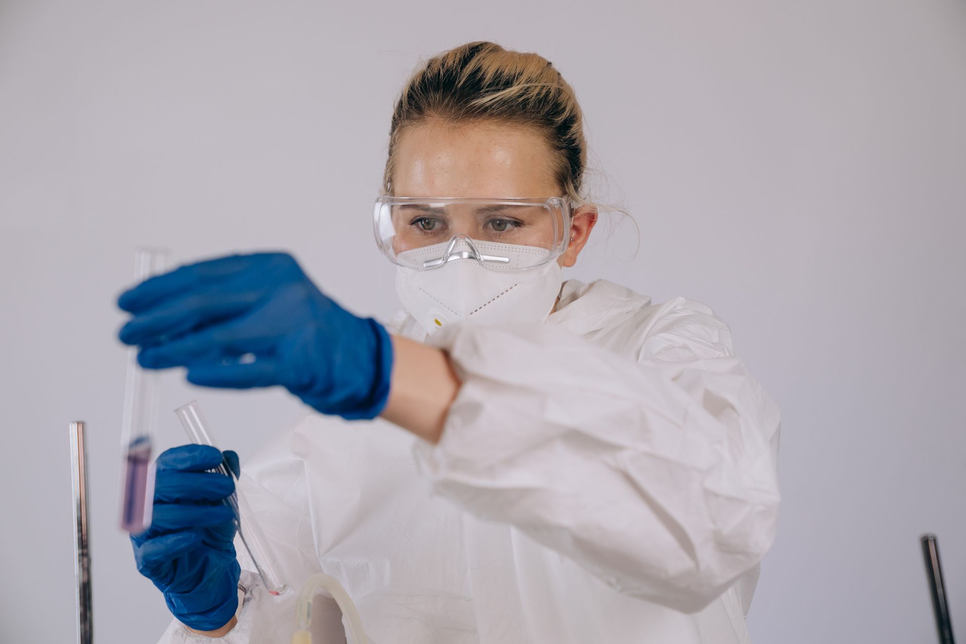 Scientist in protective gear working with test tubes in a lab environment.