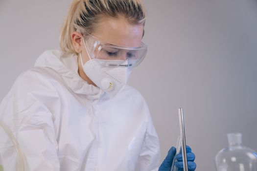 Female scientist wearing PPE conducting laboratory experiment indoors.