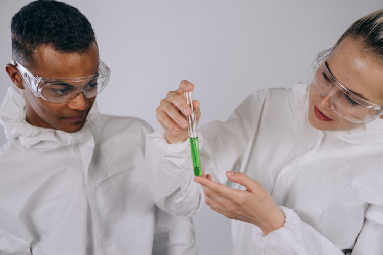 Chemists In PPE Looking At Test Tubes