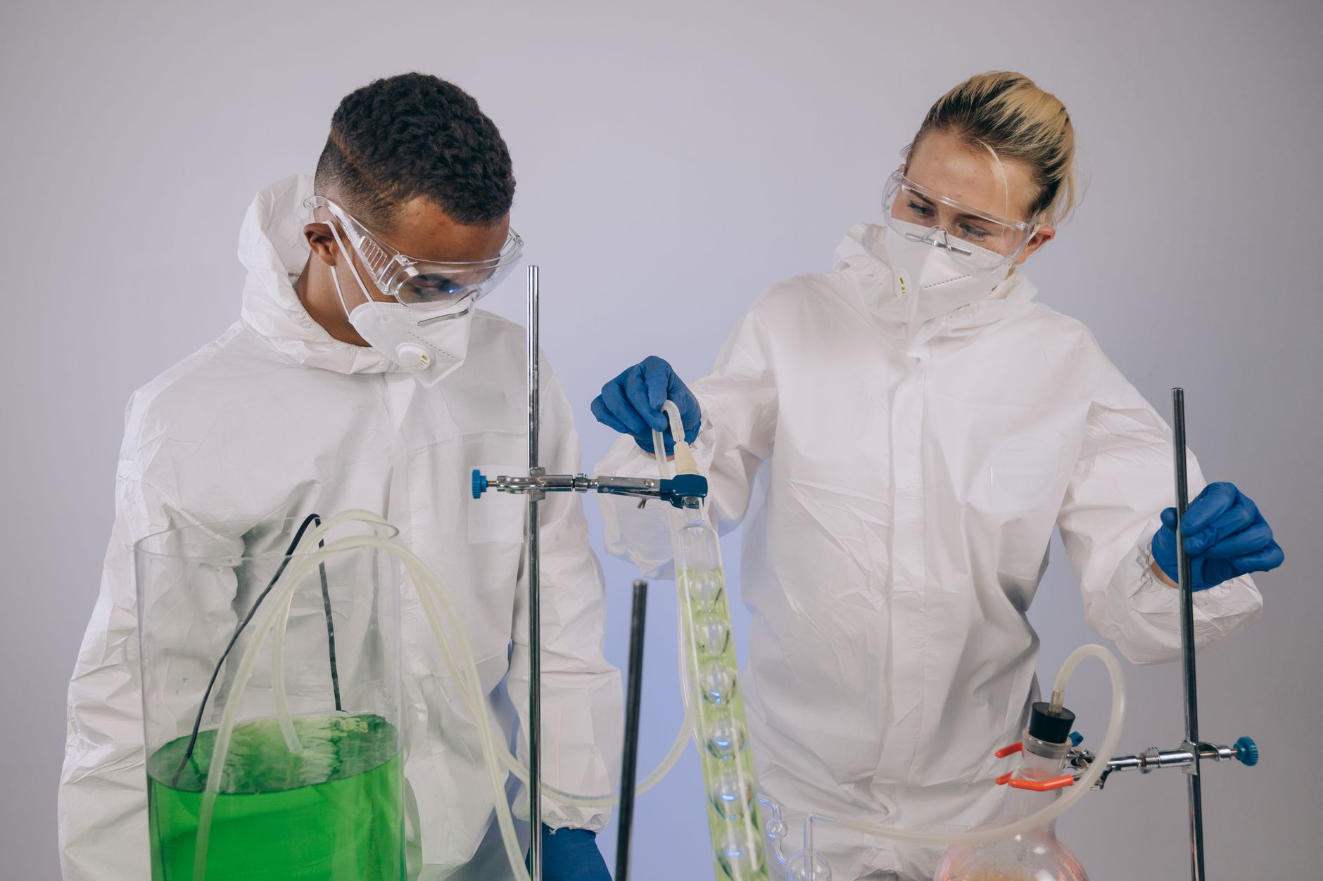 Two scientists in protective gear conducting chemical experiment with lab equipment.