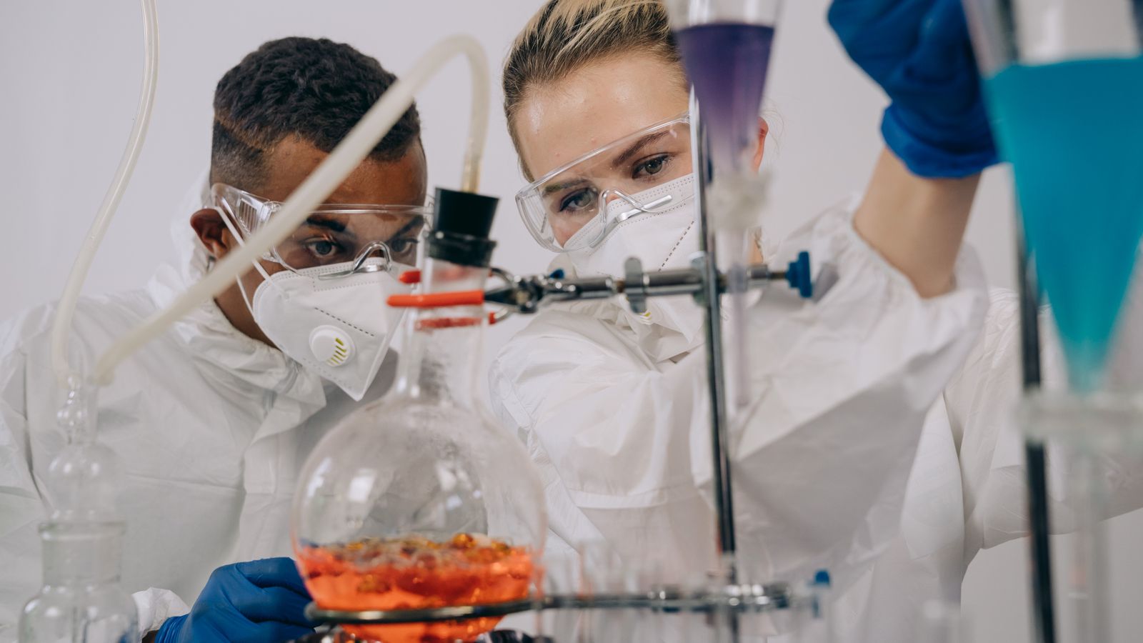 Two scientists in protective gear conducting chemistry experiments in a lab.
