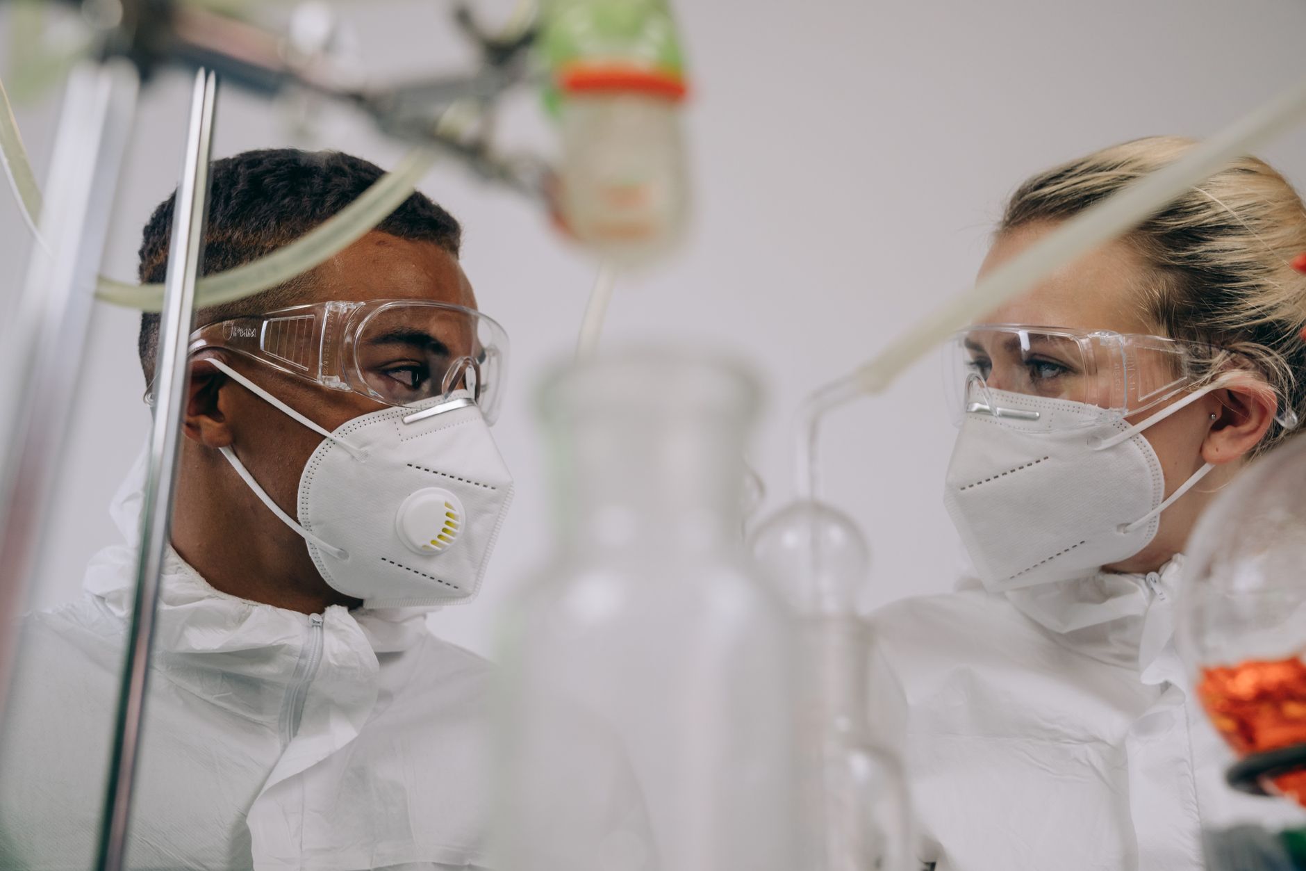 Two scientists in protective suits and masks working in a laboratory setting with equipment.