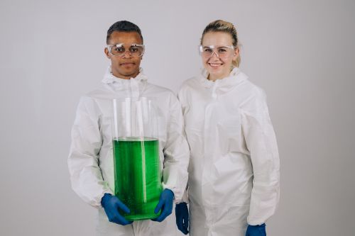 Free Two scientists in protective gear with a large green chemical vial, showcasing laboratory research. Stock Photo